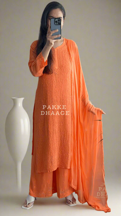 Person wearing an orange chikankari kurta set, with dupatta standing in front of a mirror.