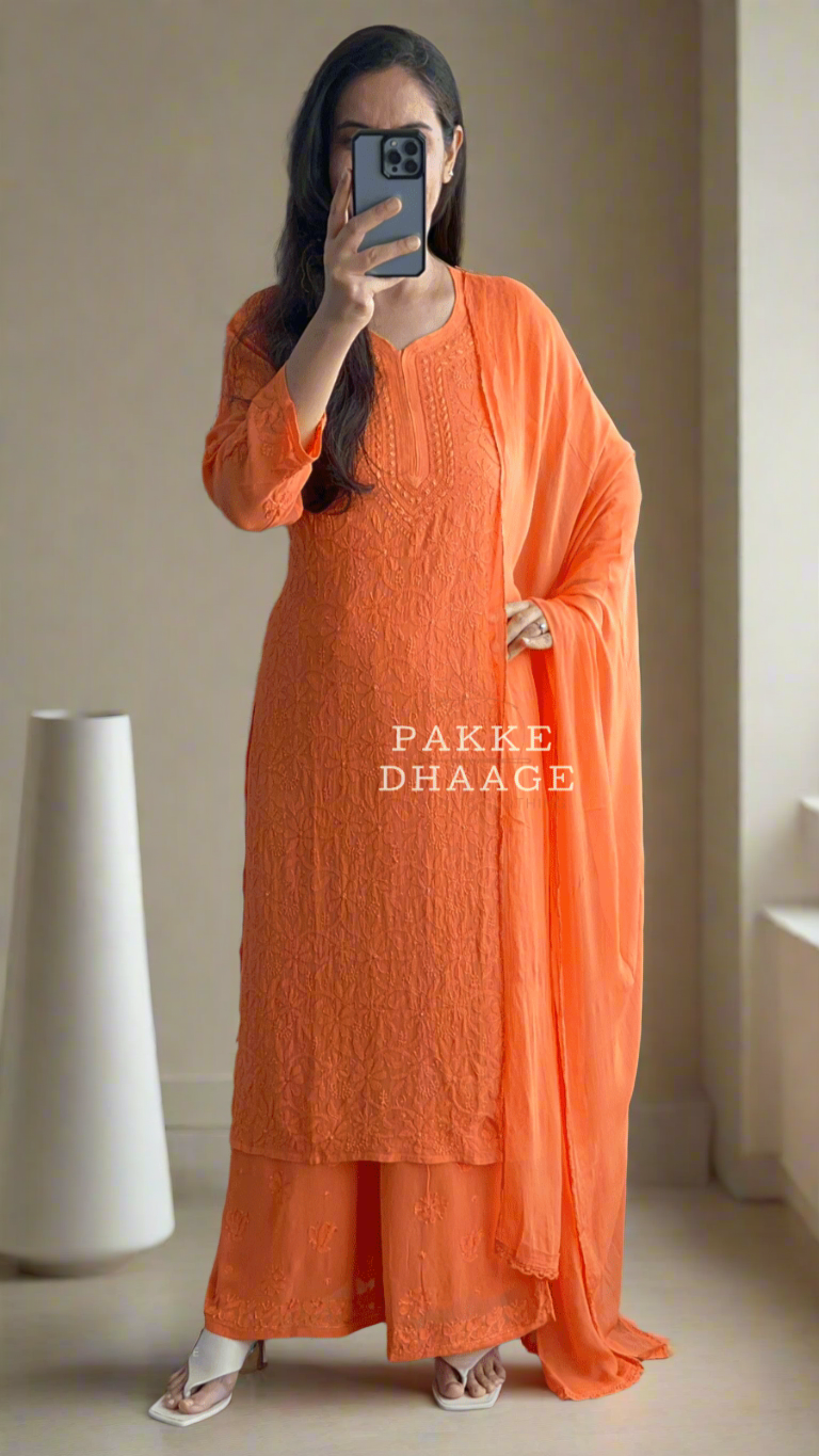 Person wearing a bright orange viscose chikankari outfit with 'PAKKI DHAAGE' branding, standing in a room with plants.
