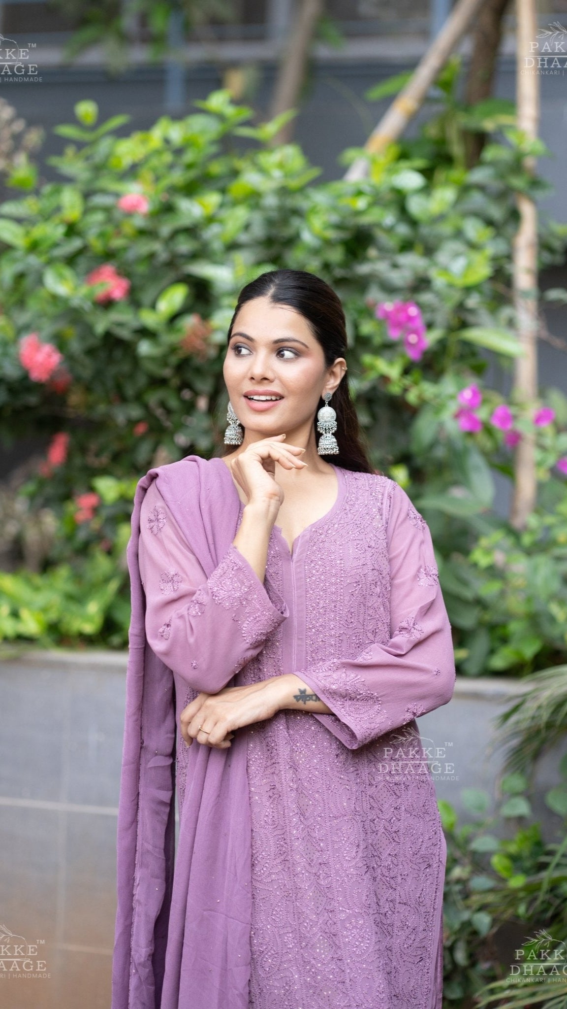 Woman in a plum chikankari suit set with hand-embroidered motifs standing in front of greenery