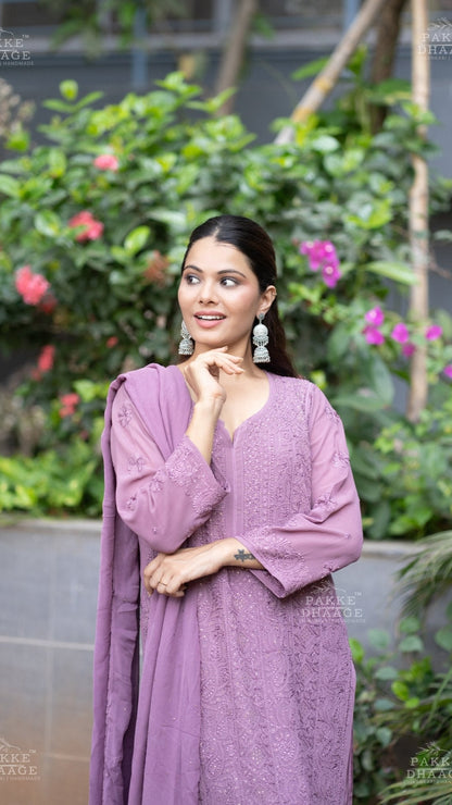 Woman in a plum chikankari suit set with hand-embroidered motifs standing in front of greenery