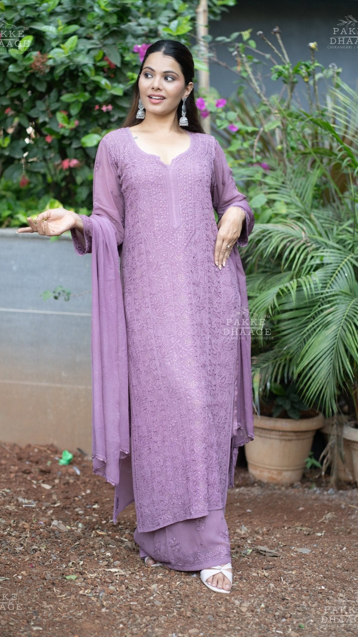 Woman in a plum chikankari traditional outfit standing outdoors with plants in the background