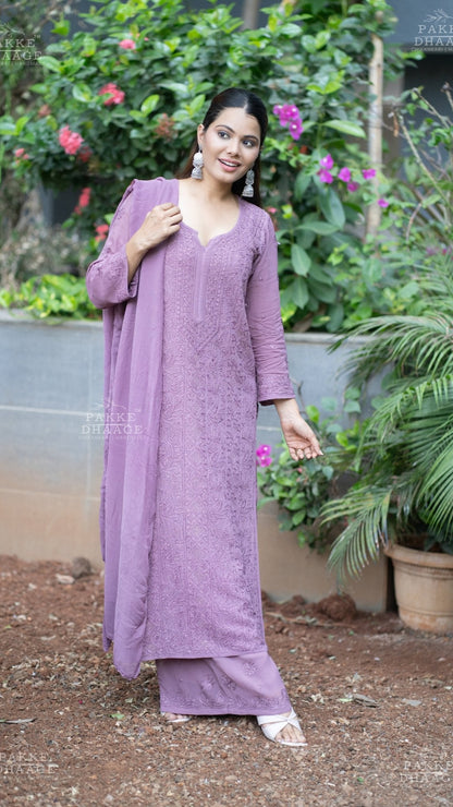 Woman in a plum chikankari hand embroidered outfit standing outdoors with greenery in the background