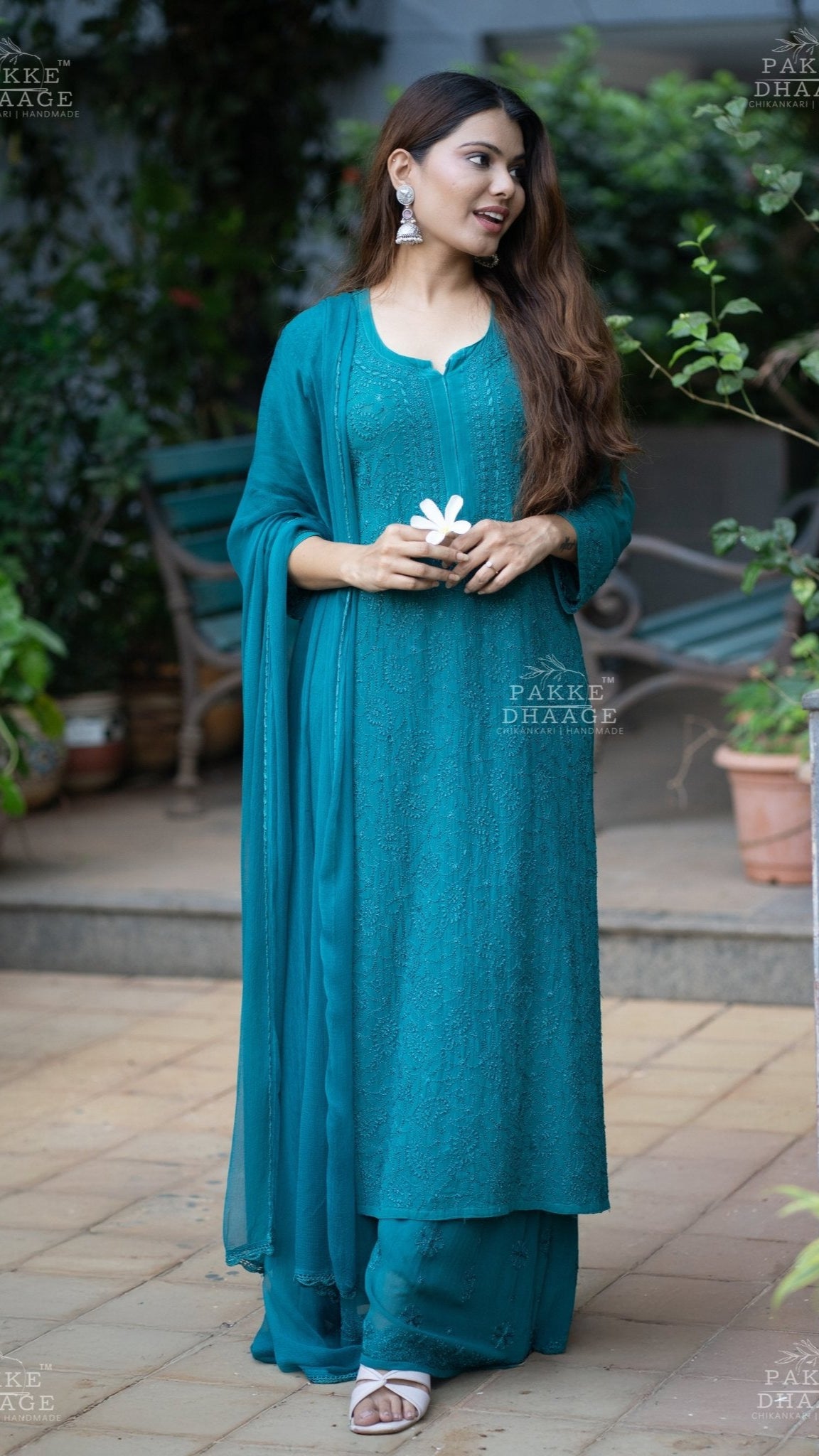 Woman in a teal chikankari viscose suit standing outdoors with plants and furniture in the background