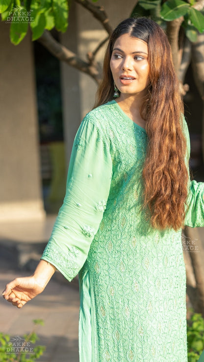 Woman in a green traditional chikankari outfit standing outdoors with trees in the background