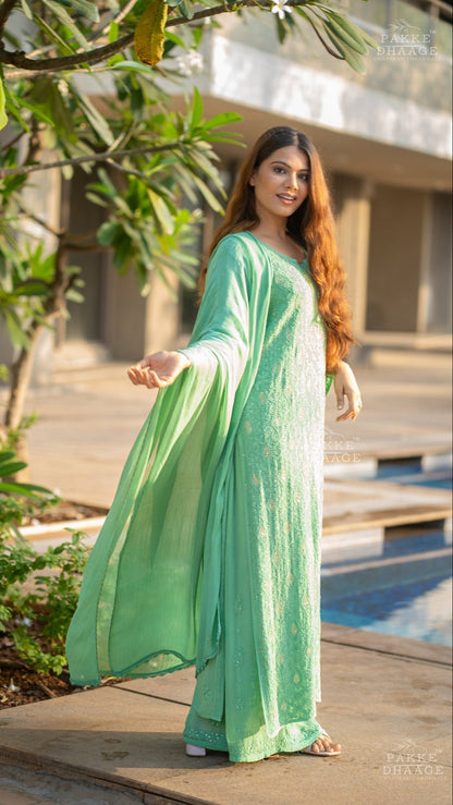Woman in a light green chikankari suit standing outdoors with plants and a building in the background
