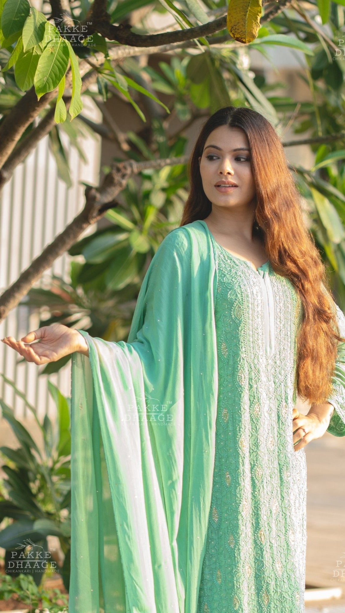 Woman in a green traditional chikankari outfit standing outdoors with greenery around.