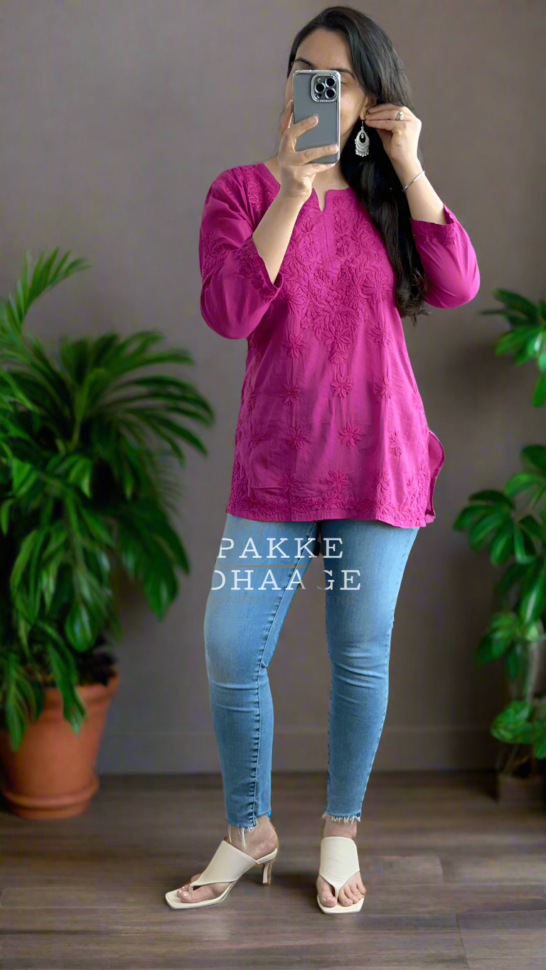 Person wearing a chikankari pink top and blue jeans in a room with plants.