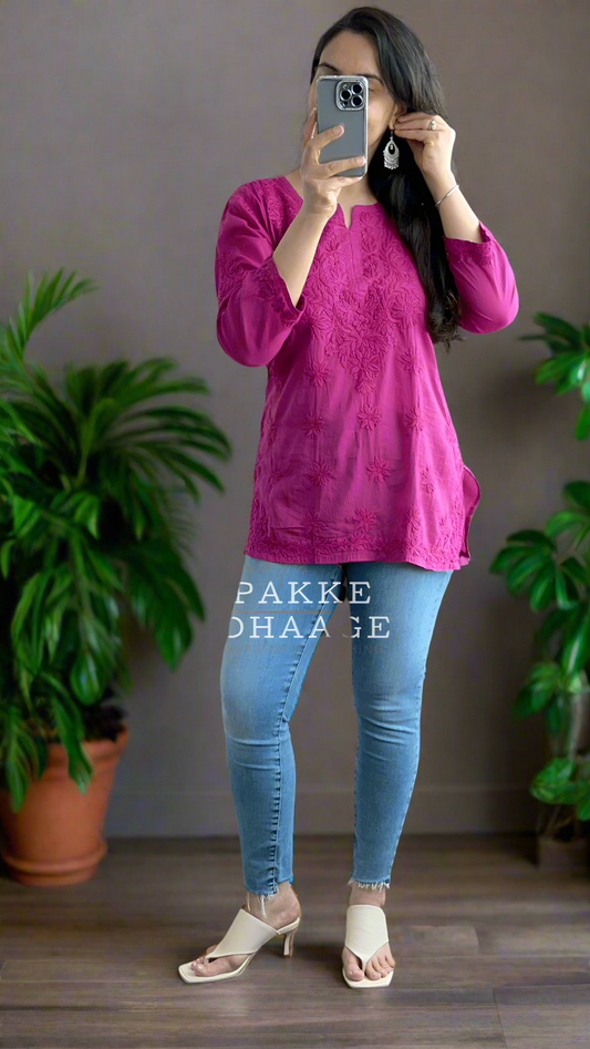 Person wearing a chikankari pink top and blue jeans in a room with plants.