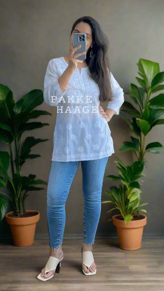 Person wearing a white chikankari top and jeans on a balcony with plants.