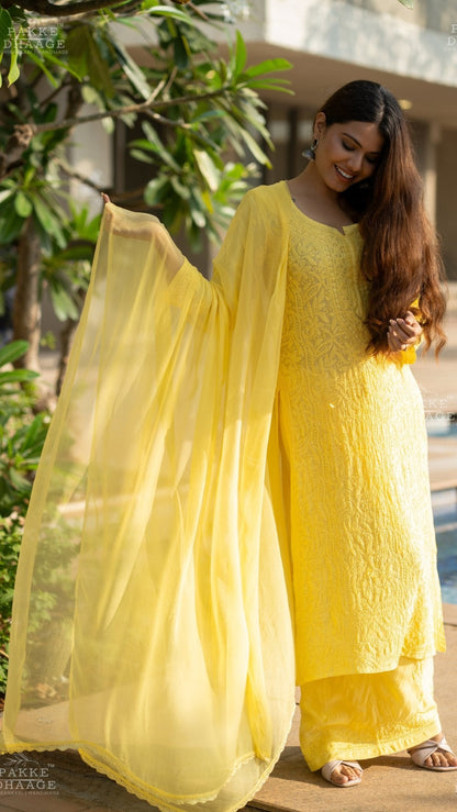 Woman in a bright yellow traditional chikankari Kurti Set standing by a poolside with greenery in the background