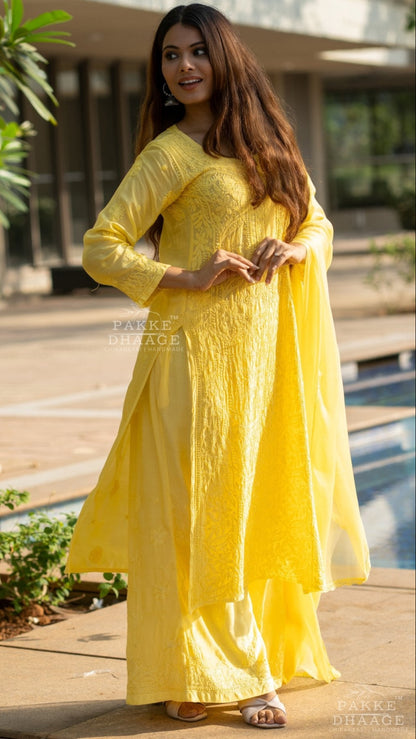 Woman in a yellow hand-embroidered Chikankari set standing outdoors near a pool.