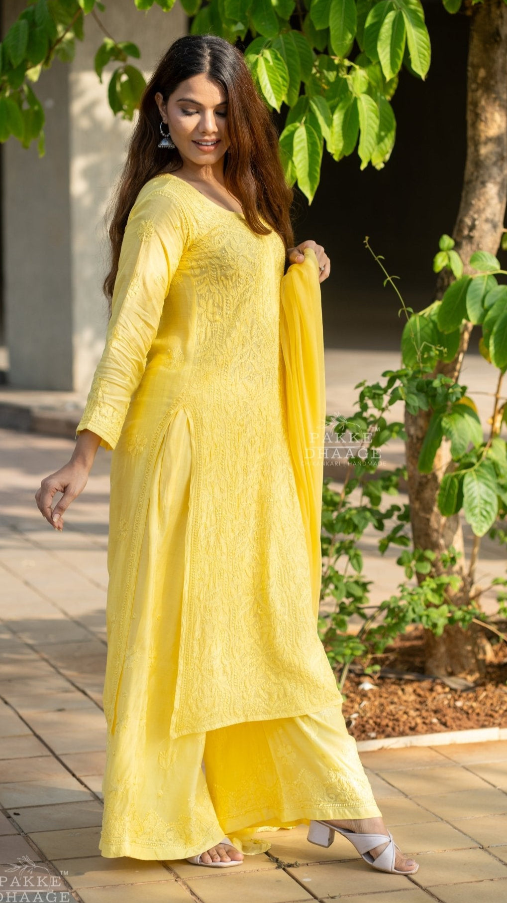Woman in a yellow handmade chikankari suit set standing outdoors with greenery around