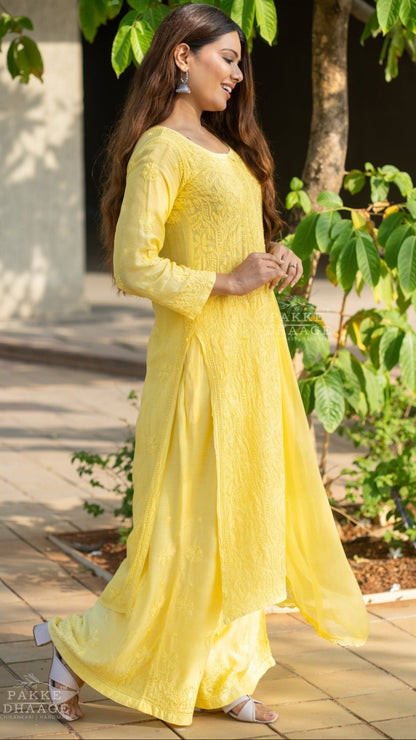 Woman in a yellow chikankari suit with hand-embroidered motifs standing outdoors with greenery around