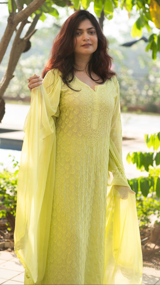 close-up shot of a Woman in a lemon yellow chikankari kurti set, with matching dupatta standing outdoors with greenery around