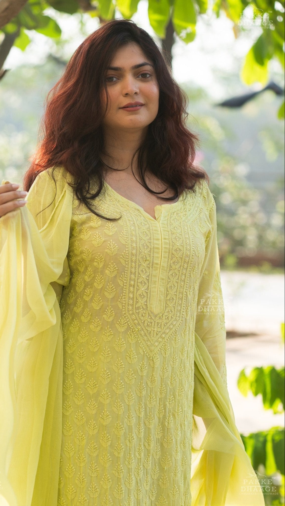 Woman wearing a lemon yellow traditional chikankari set with a green leafy background