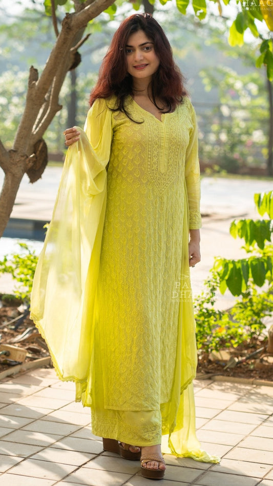 Woman in a lemon yellow handmade chikankari kurti set standing outdoors with greenery around.