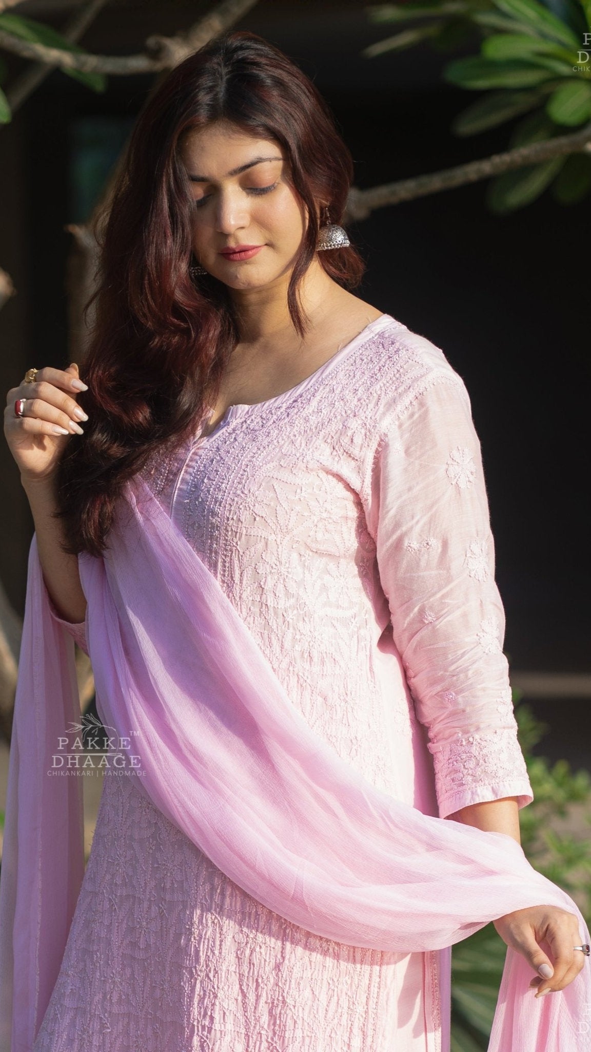 Woman wearing a light pink traditional chikankari suit with a matching dupatta, standing outdoors.