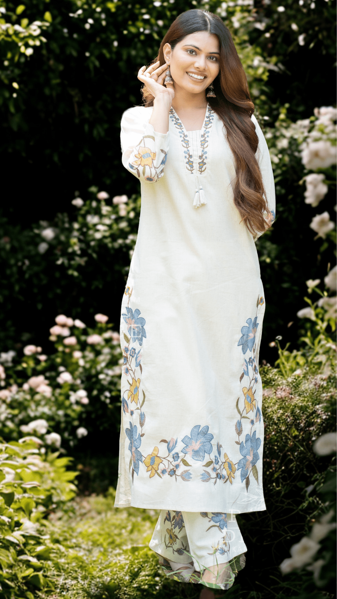 Woman in a white printed suit set standing in a garden with flowers.