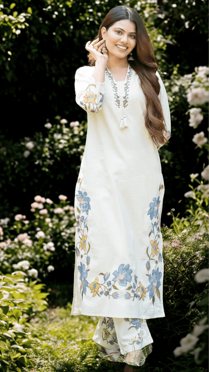 Woman in a white printed suit set standing in a garden with flowers.