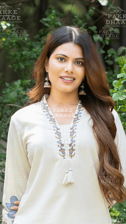 Woman wearing a white suit set with printed pattern on neckline against a green leafy background