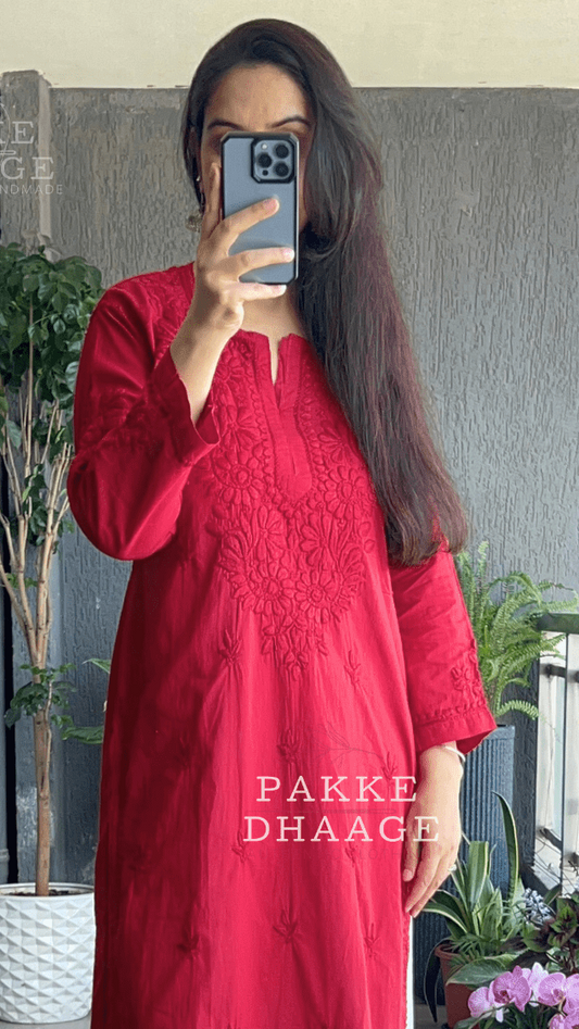 Person wearing a red chikankari kurta in front of a mirror with plants in the background.