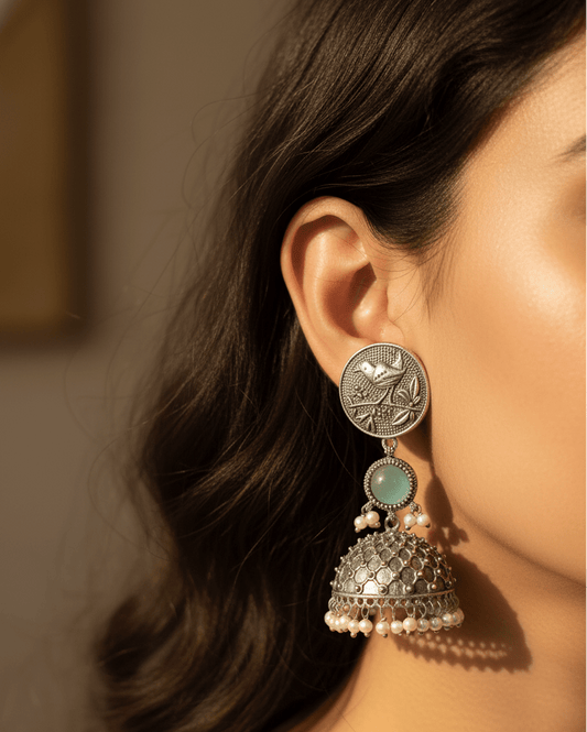 Close-up of a woman wearing a silver and turquoise earring with pearl accents.