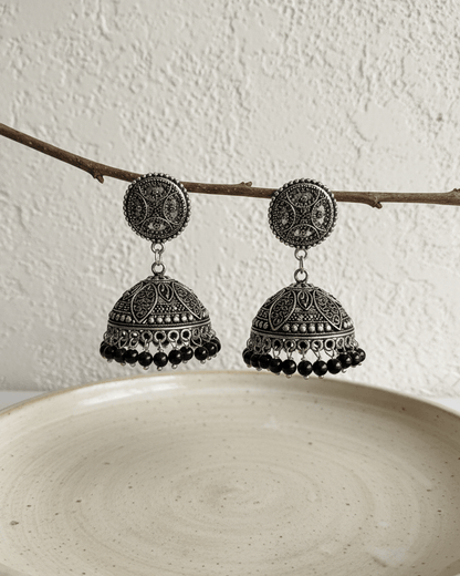 Pair of silver and black earrings on a branch against a white background