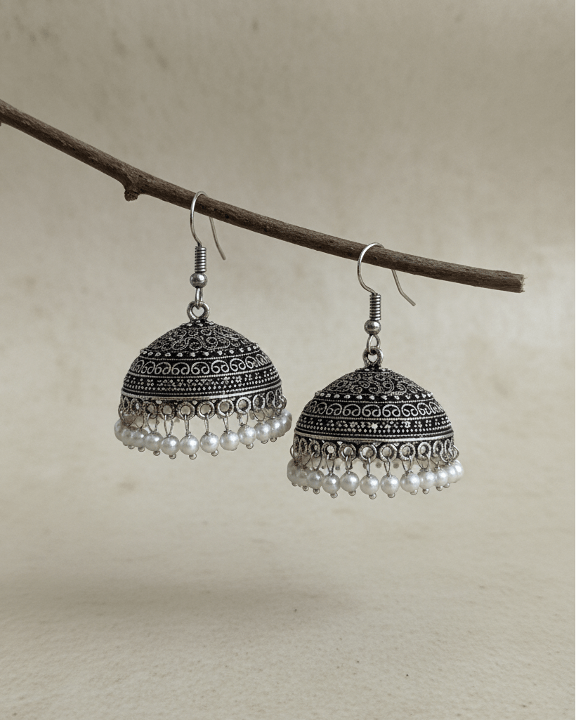 Pair of silver earrings with pearl-like beads hanging from a branch on a neutral background