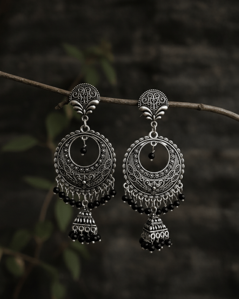 Pair of silver oxidised earrings hanging on a branch with a dark background