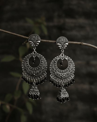 Pair of silver oxidised earrings hanging on a branch with a dark background