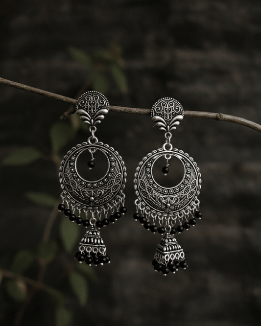 Pair of silver oxidised earrings hanging on a branch with a dark background