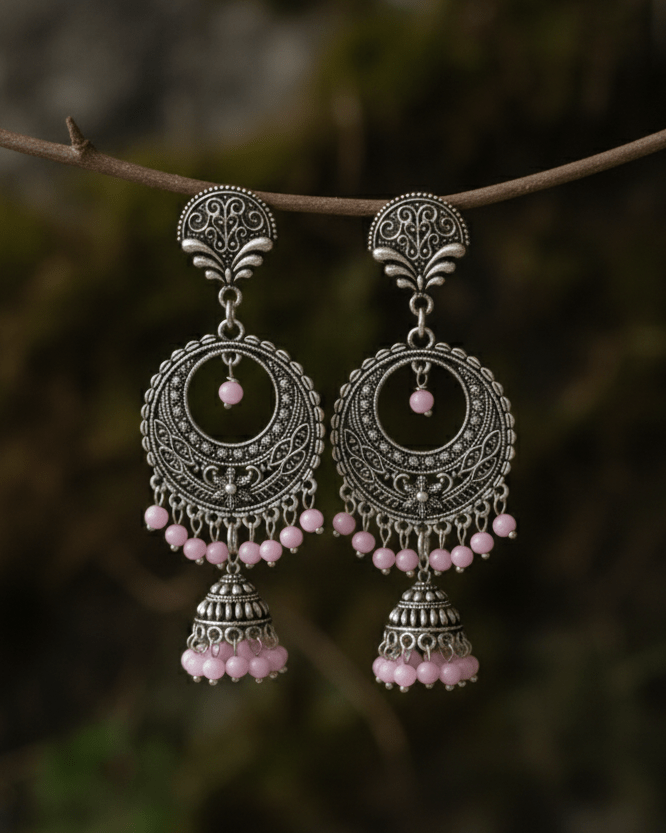 Ornate silver oxidized earrings with pink beads on a branch against a blurred natural background