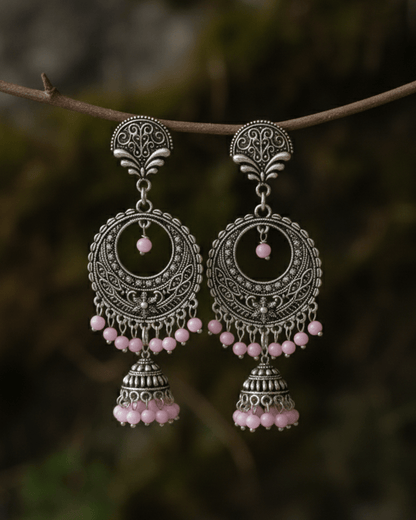 Ornate silver oxidized earrings with pink beads on a branch against a blurred natural background