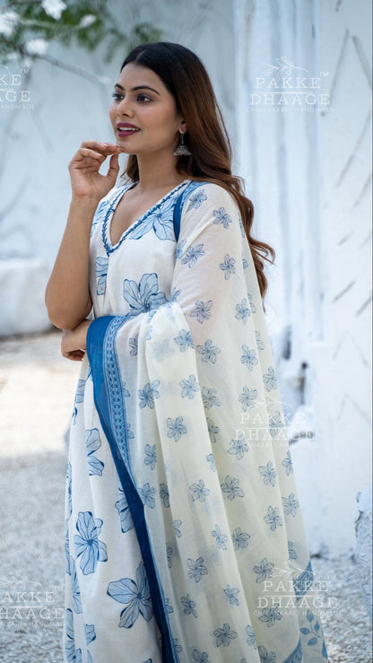 Woman wearing an off-white suit-set with blue floral patterns, standing against a white background.
