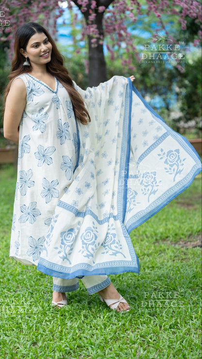 Woman in a white and blue floral printed suit set standing outdoors with greenery and cherry blossoms in the background.