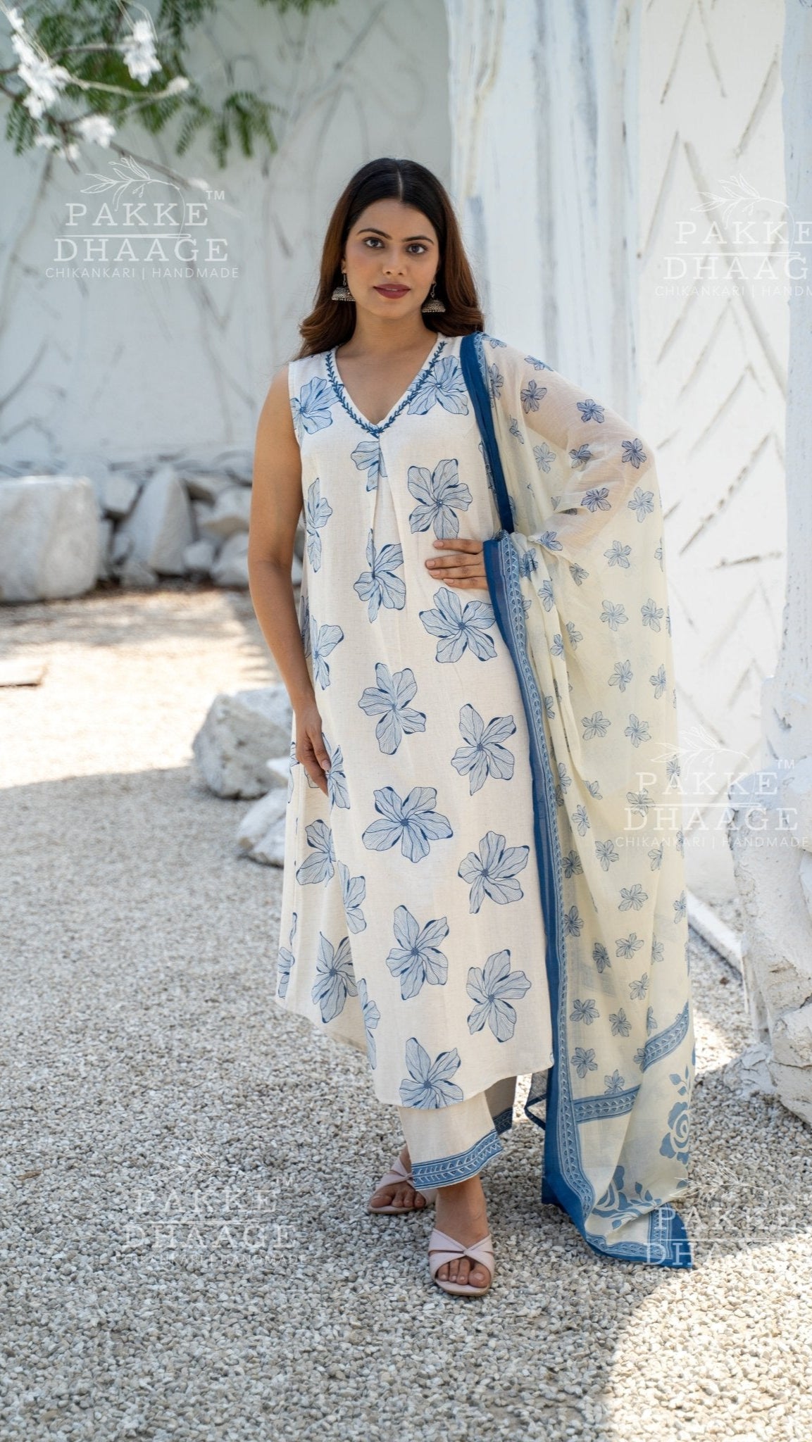 Woman in a floral, sleeveless kurti set standing outdoors with white architectural elements in the background