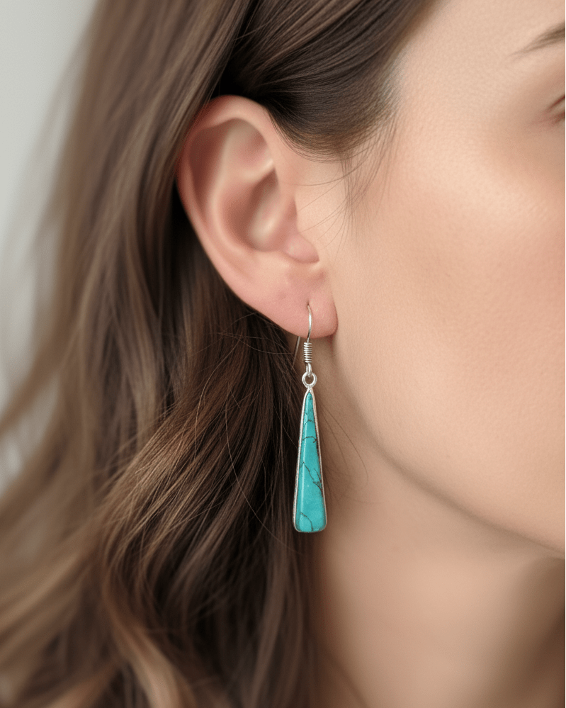Close-up of a woman wearing turquoise teardrop earrings with a neutral background