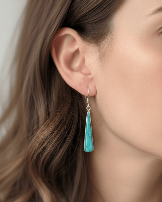 Close-up of a woman wearing turquoise teardrop earrings with a neutral background