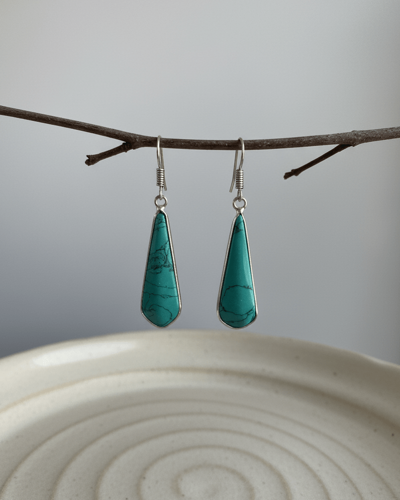 Teal drop earrings hanging from a branch on a white plate with a gray background