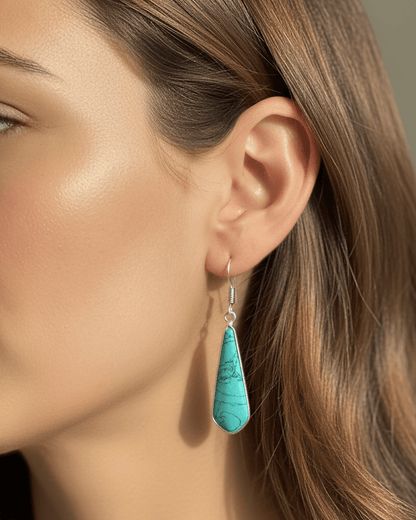 Close-up of a turquoise teardrop earring worn by a person with brown hair.