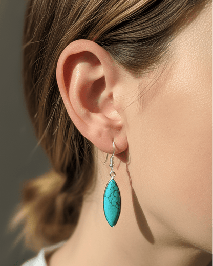 Close-up of a person wearing turquoise earrings with a neutral background