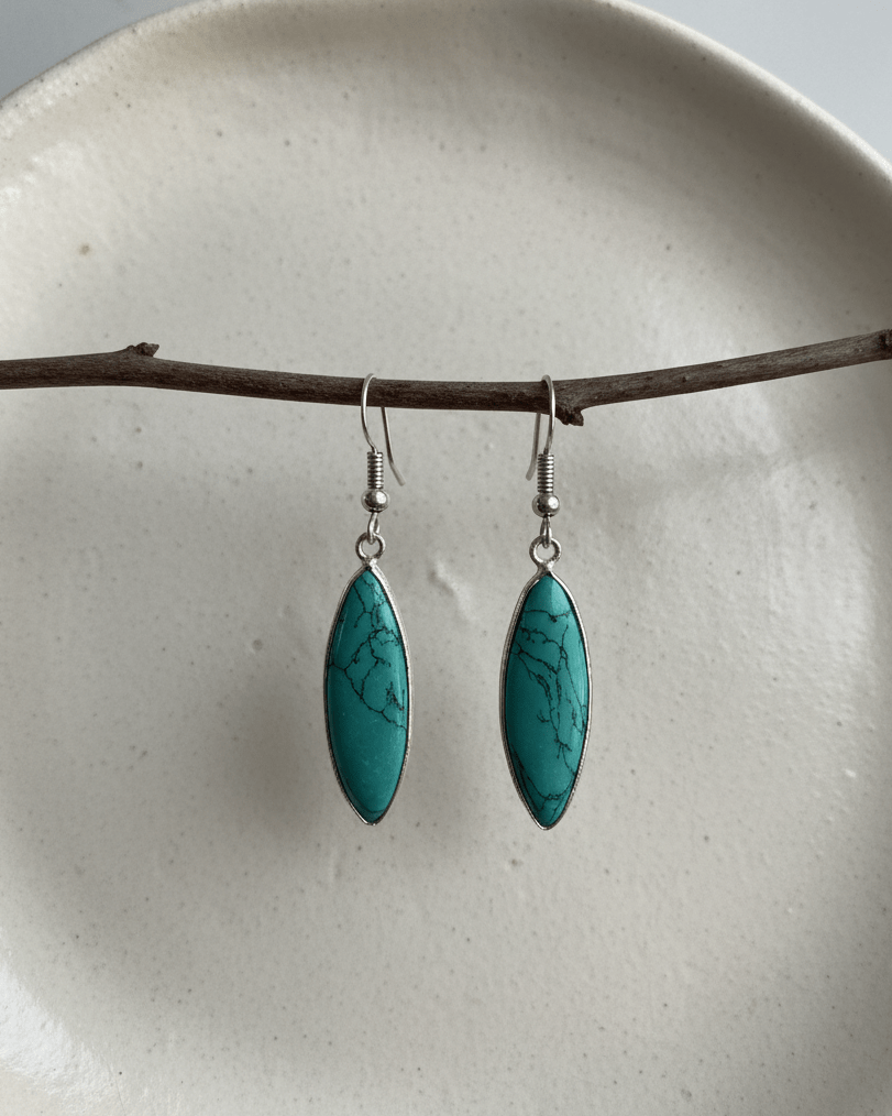 Turquoise earrings hanging from a branch on a white plate