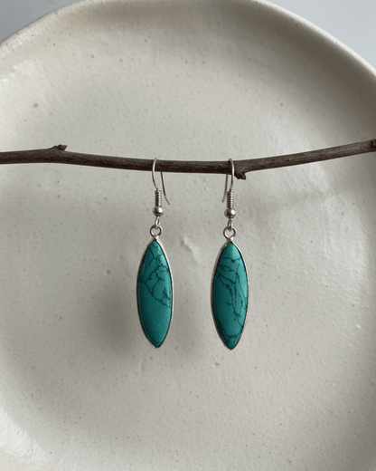 Turquoise earrings hanging from a branch on a white plate