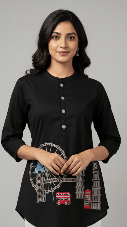 Woman wearing a black top with London-themed embroidery on a gray background
