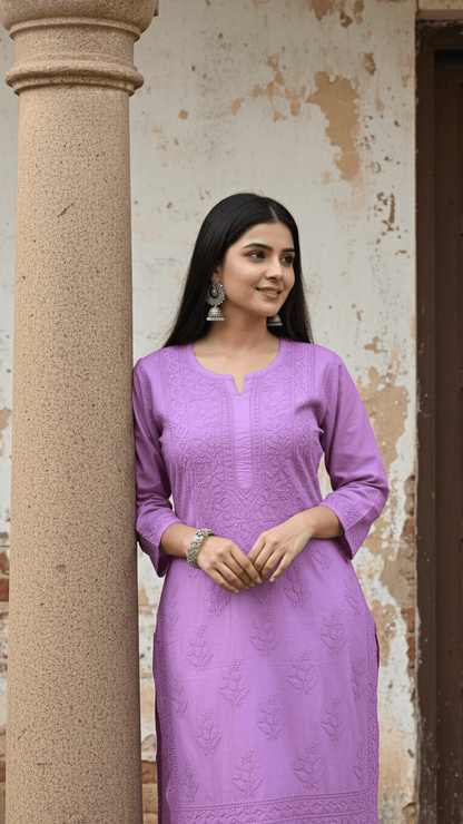 Woman in a mauve chikankari kurta standing against a textured wall.