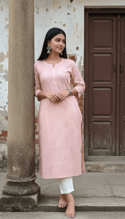 Woman wearing a mocha chikankari kurta with white pants standing against a rustic wall.