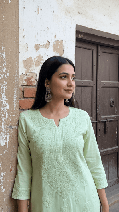 Woman in a light green kurta standing against a textured wall.